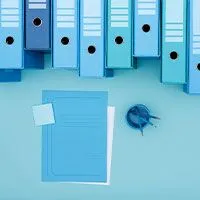 Blue office binders, notepad, and paperclip on blue background.