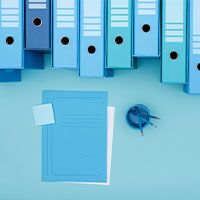 Blue office binders, notepad, and paperclip on blue background.